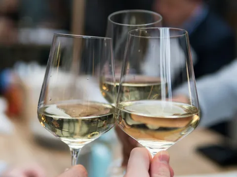Brindis con copas de vino blanco, enfoque cercano en las manos y el cristal.