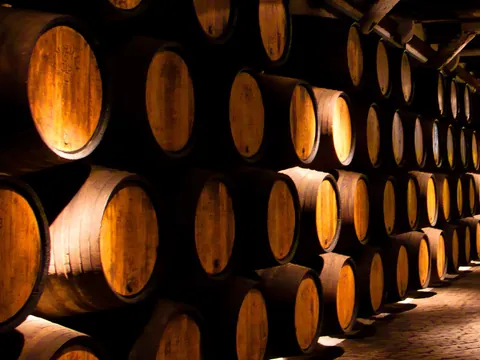 Sala de barricas de vino apiladas en una bodega iluminada cálidamente.