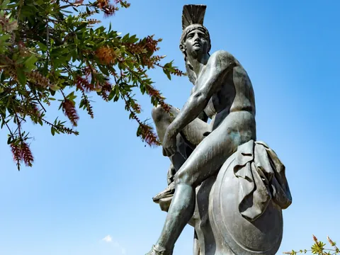 Estatua de guerrero griego con casco y escudo bajo un cielo azul en Atenas