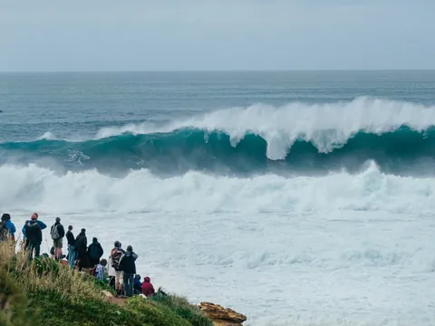 Turistas observando una ola gigante rompiendo en la costa de Nazaré, Portugal.
