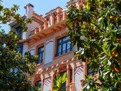 Fachada modernista de un edificio histórico en Gijón entre árboles frondosos.