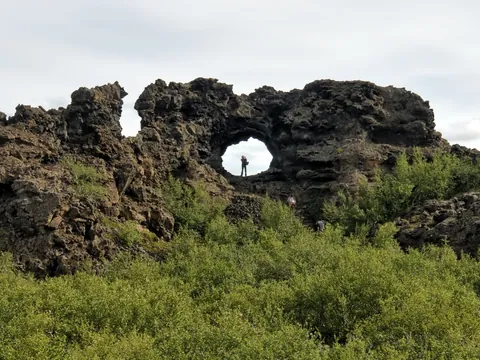Formaciones de lava en Dimmuborgir, Islandia, con arco natural de roca volcánica rodeado de vegetación verde.