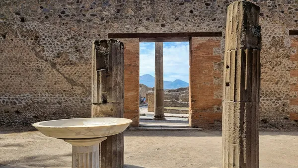 Ruinas arqueológicas de Pompeya con columnas y estructuras romanas, al fondo el monte Vesubio bajo cielo despejado."