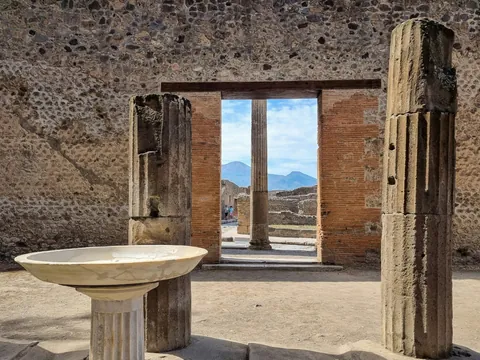 Ruinas arqueológicas de Pompeya con columnas y estructuras romanas, al fondo el monte Vesubio bajo cielo despejado."