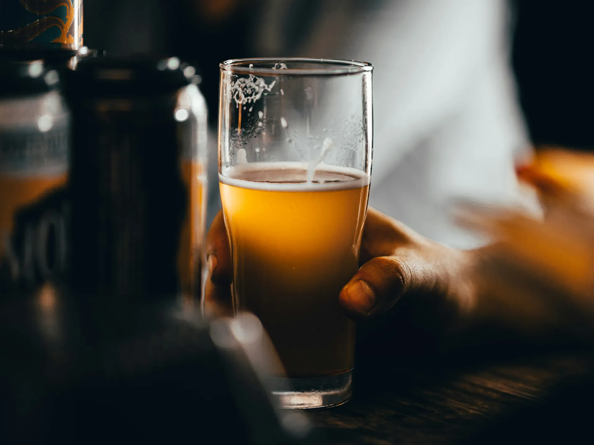 Mano sosteniendo vaso de cerveza artesanal en un bar de Brujas