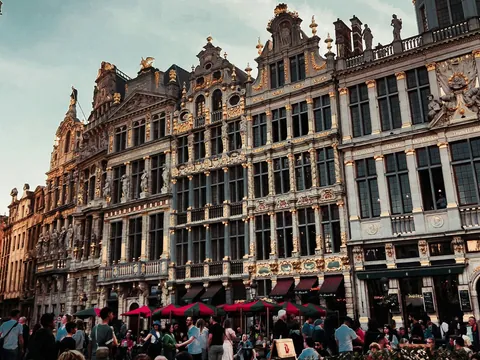 Personas disfrutando en terrazas al aire libre frente a los históricos y ornamentados edificios de la Grand Place de Bruselas.