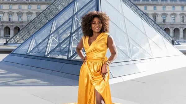 Persona con vestido largo amarillo posando frente a la Pirámide del Louvre en París.