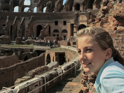 Niña observando el interior del Coliseo de Roma desde un mirador entre ruinas