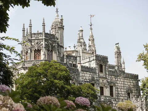 Fachada ornamentada de la Quinta da Regaleira en Sintra rodeada de árboles y flores.