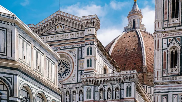 Detalle arquitectónico de la Catedral de Santa María del Fiore en Florencia, Italia, mostrando la fachada con mármol policromado y la cúpula de Brunelleschi bajo un cielo azul.