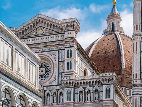 Detalle arquitectónico de la Catedral de Santa María del Fiore en Florencia, Italia, mostrando la fachada con mármol policromado y la cúpula de Brunelleschi bajo un cielo azul.