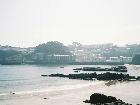Playa de Luarca, Asturias, con rocas oscuras, arena y el pueblo costero en el horizonte.