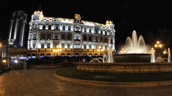 Fuente iluminada de la Plaza de la Escandalera en Oviedo frente al edificio histórico del Banco Herrero, una vista nocturna emblemática.
