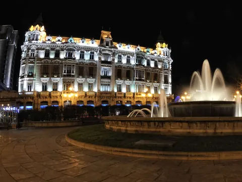 Fuente iluminada de la Plaza de la Escandalera en Oviedo frente al edificio histórico del Banco Herrero, una vista nocturna emblemática.
