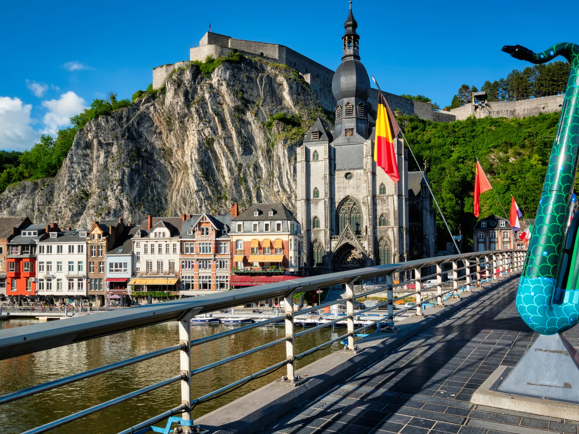 Escultura de saxofón en puente de Dinant con la Colegiata y ciudadela al fondo