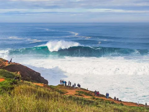 Gente observando una ola gigante rompiendo en los acantilados de Nazaré, Portugal