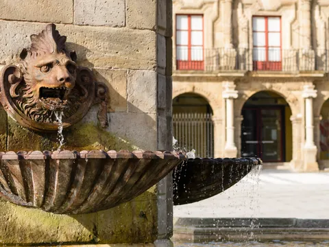 Fuente del Monumento a Pelayo con detalle escultórico en piedra y fachada del Palacio de Revillagigedo en Gijón.