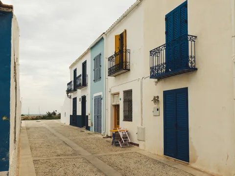 Calle empedrada de Tabarca con casas blancas y contraventanas azules y amarillas bajo un cielo nublado.