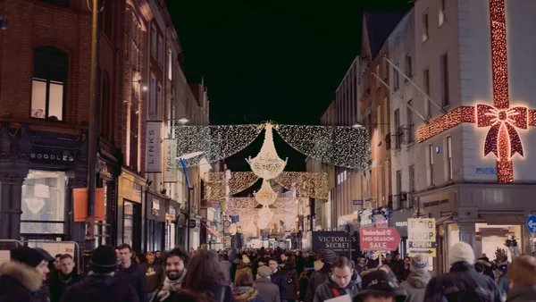 Calle de Dublín decorada con luces navideñas y adornos en la noche, con numerosos peatones paseando y tiendas iluminadas a ambos lados.