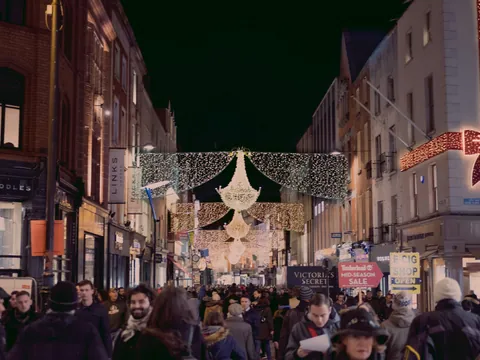 Calle de Dublín decorada con luces navideñas y adornos en la noche, con numerosos peatones paseando y tiendas iluminadas a ambos lados.