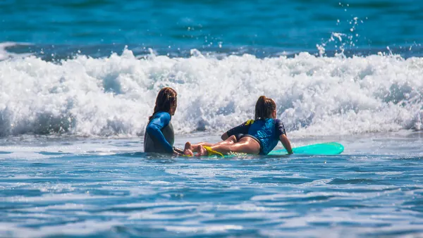 Profesor ayudando a una niña sobre su tabla de surf en el mar de Mundaka, Vizcaya