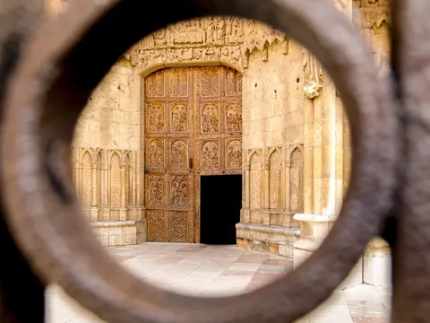 Puerta de madera tallada de la Catedral de León, estilo gótico, vista a través de una reja o mirilla de hierro forjado.
