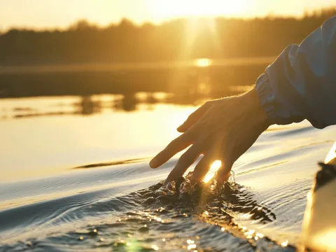 Mano rozando el agua desde un kayak al atardecer en Es Grau, Menorca