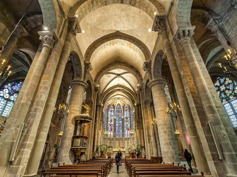 Interior gótico de la Basílica de San Nazario en Carcasona, con vitrales, columnas y bancos de madera.