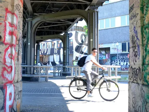 Ciclista pasando bajo una estructura de hierro con grafiti en Berlín.