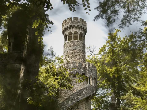 Torre de piedra con escalera en espiral entre árboles en los jardines de la Quinta da Regaleira.