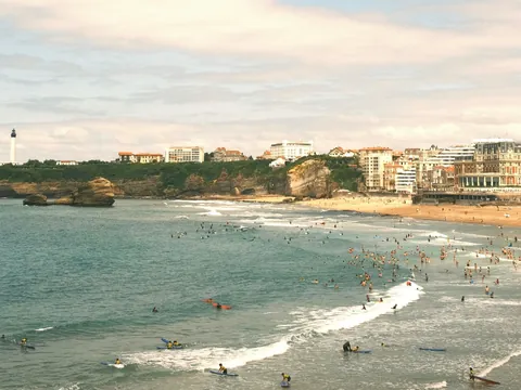 Playa de Biarritz con surfistas en el agua y edificios junto a la costa.