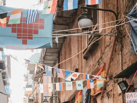 Banderas italianas decorando callejón del Barrio Español de Nápoles entre edificios antiguos