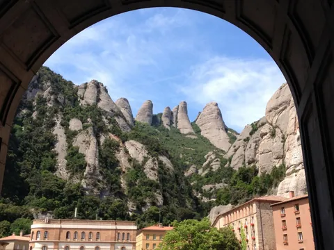 Vista enmarcada por un arco desde el monasterio de Montserrat hacia los picos rocosos, cubiertos de vegetación.