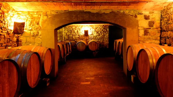 Bodega tradicional en la Toscana, Italia, con barricas de madera alineadas en una sala de piedra iluminada con luz cálida.