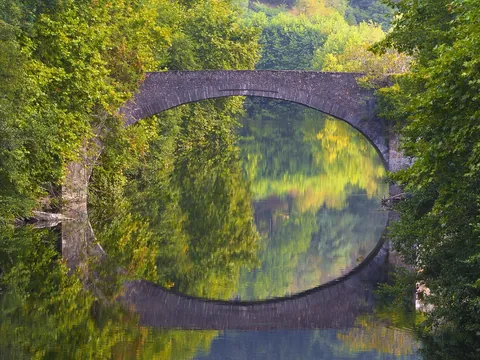 Puente de piedra reflejado en el río rodeado de vegetación en Bera, creando un arco perfecto.