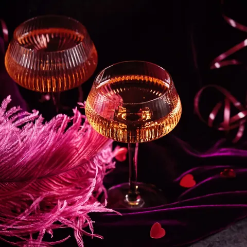 Dos copas de champán sobre terciopelo púrpura con plumas rosas en París