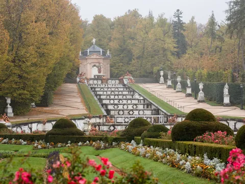 La Cascada Nueva de La Granja rodeada de árboles otoñales y estatuas blancas.