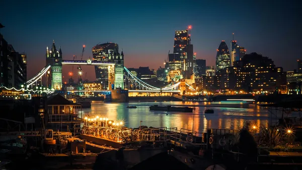 Puente de la Torre iluminado y rascacielos del City de Londres al anochecer.