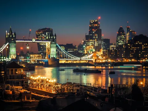 Puente de la Torre iluminado y rascacielos del City de Londres al anochecer.