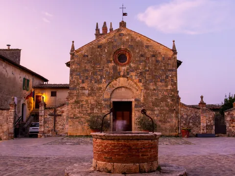 Plaza con iglesia medieval y fuente al atardecer en la Toscana, Italia