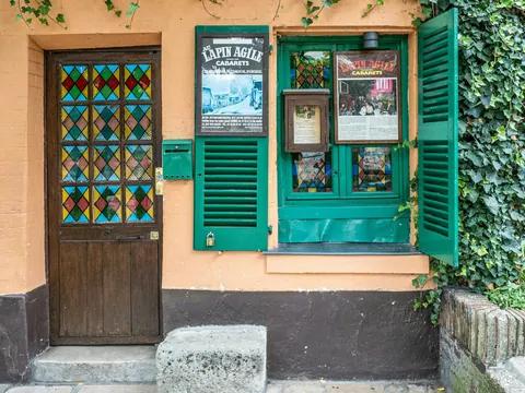 Entrada decorada de un bar en Montmartre, París, con objetos artísticos colgados en la pared, puerta ornamentada y macetas en una calle empedrada bajo luz natural.