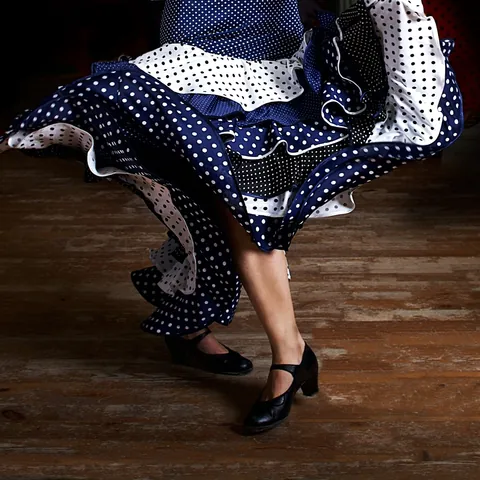Mitad inferior de una mujer bailando flamenco sobre un tablao flamenco vestida de sevillana, España
