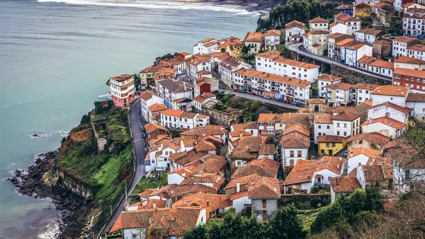 Panorámica de Lastres, Asturias, pueblo marinero de casas con tejados naranjas en un acantilado costero.