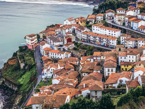 Panorámica de Lastres, Asturias, pueblo marinero de casas con tejados naranjas en un acantilado costero.