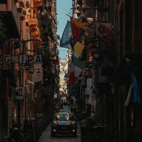 Calle estrecha y oscura de los Quartieri Spagnoli (Barrios Españoles) en Nápoles, Italia, con banderas colgantes.