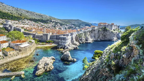 Murallas de Dubrovnik bordeando la costa, acantilados y aguas turquesas desde un punto elevado.