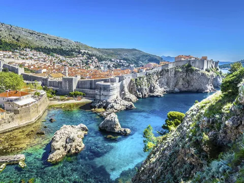 Murallas de Dubrovnik bordeando la costa, acantilados y aguas turquesas desde un punto elevado.