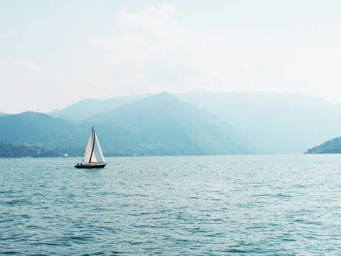 Velero navegando en el Lago di Como con montañas en el horizonte