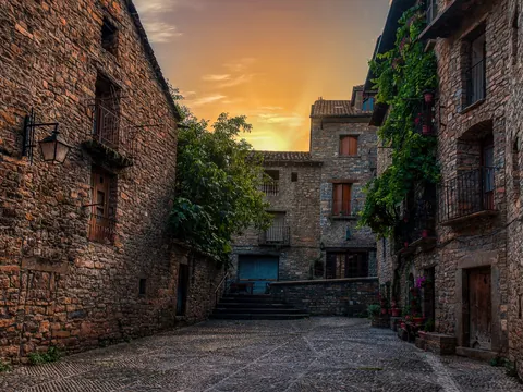 Calle empedrada rodeada de casas de piedra con balcones en la villa medieval de Aínsa.