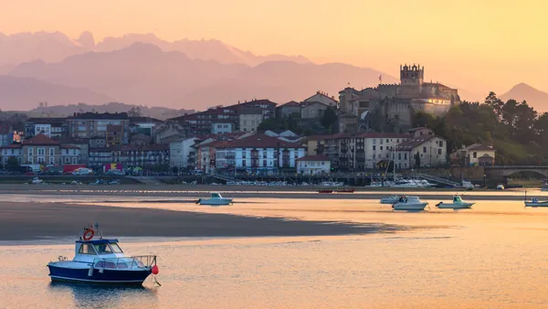 Vista de San Vicente de la Barquera al atardecer, con la iglesia y el castillo sobre el casco histórico junto a la ría.